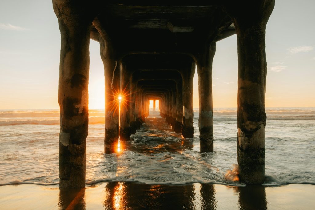 Sunset shines through pier columns on the beach.