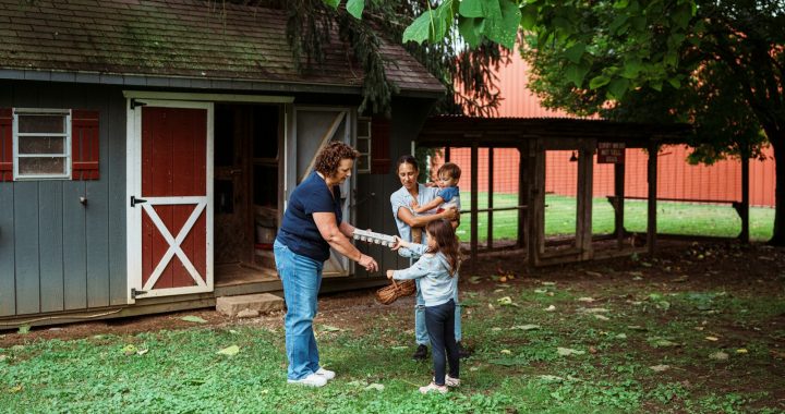 Family interacts with a woman near a shed.