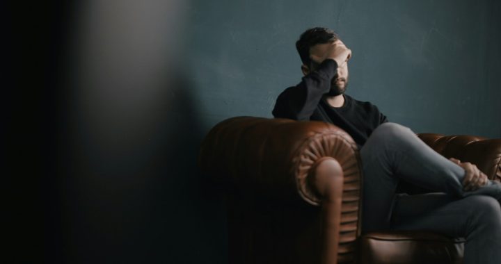 a man holds his head while sitting on a sofa